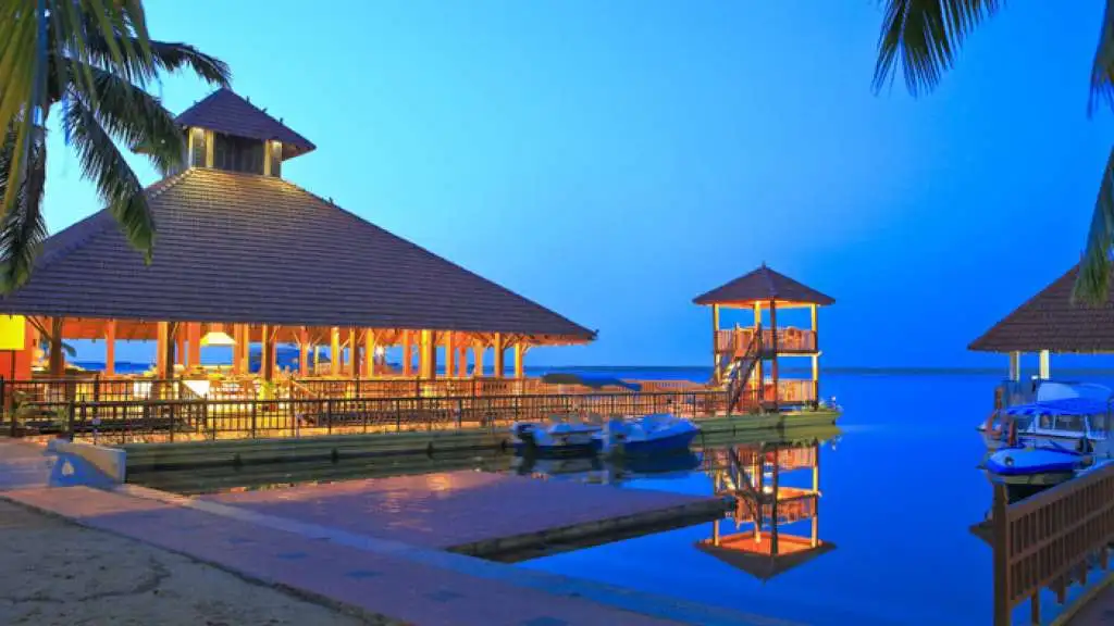 Traditional thatched roof floating restaurant lit up at night on the calm backwaters of Poovar