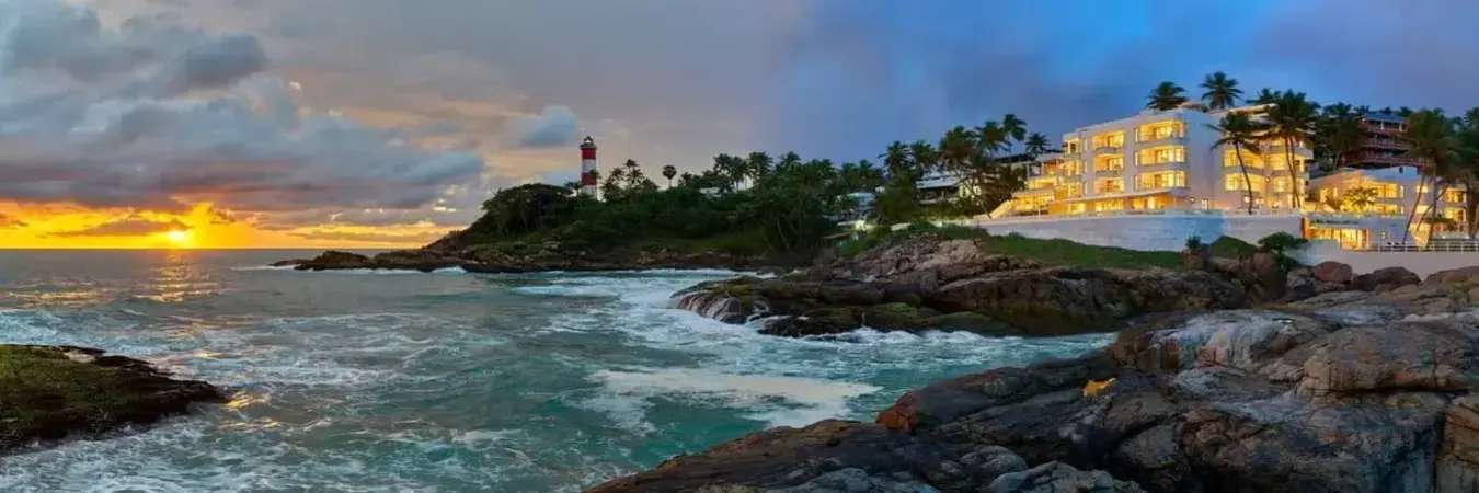 Multi-story building of Hotel Rockholm at the Lighthouse Beach Kovalam lit up at dusk next to the iconic rocky coastline.