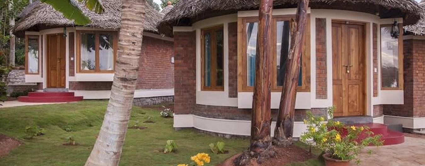 Traditional Kerala wooden cottages surrounded by green garden lawn at Somatheeram Ayurvedic Health Resort