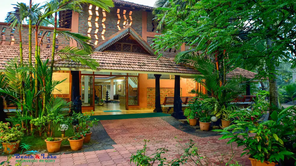 Traditional Kerala style resort building with a red tiled gabled roof and stone courtyard at Beach and Lake Ayurvedic Resort Kovalam.