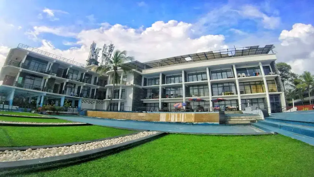 Modern multi-story building of The Neelakanta Beach Resort Kovalam with an outdoor infinity swimming pool and green lawn.