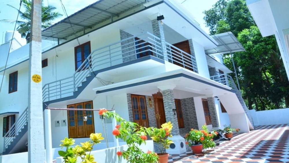 Multi-story modern white building of Bougainvillea Homestay Kovalam featuring private balconies and vibrant potted flowers.