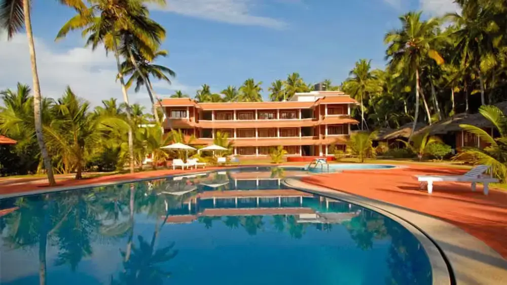 Multi-story building of Abad Harmonia Kovalam with traditional sloped roofs fronted by a large outdoor swimming pool.