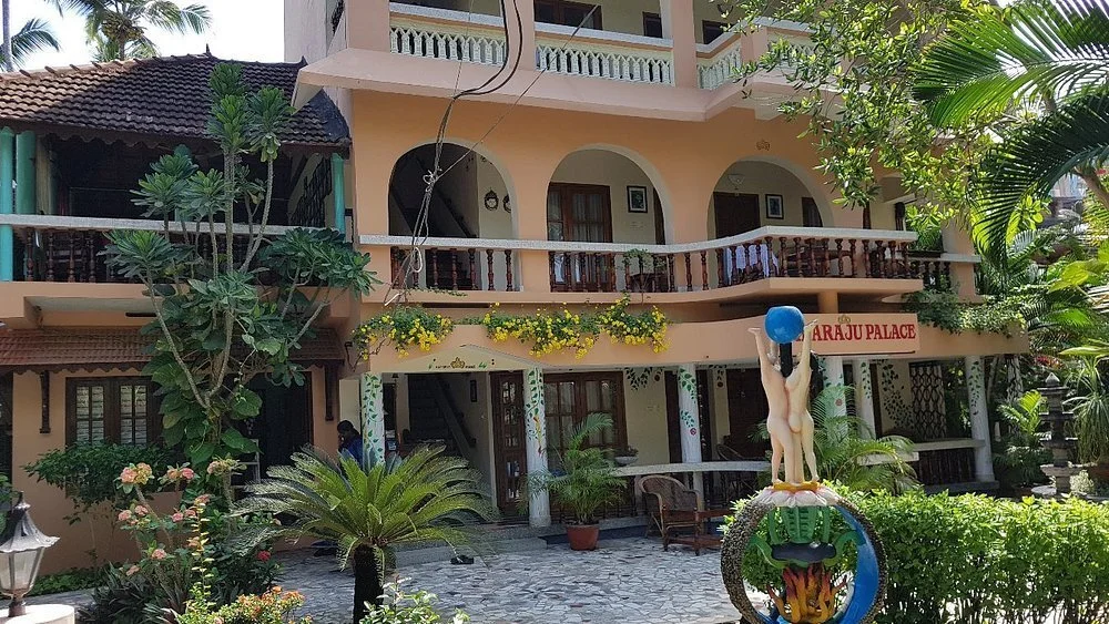 Multi-story building of Maharaju Palace Kovalam featuring arched balconies, guest verandas, and a tropical garden entrance.