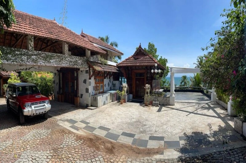 Traditional Kerala style building of Thayil Kadaloram Homestay Kovalam featuring clay tiled roofs and a paved courtyard driveway.