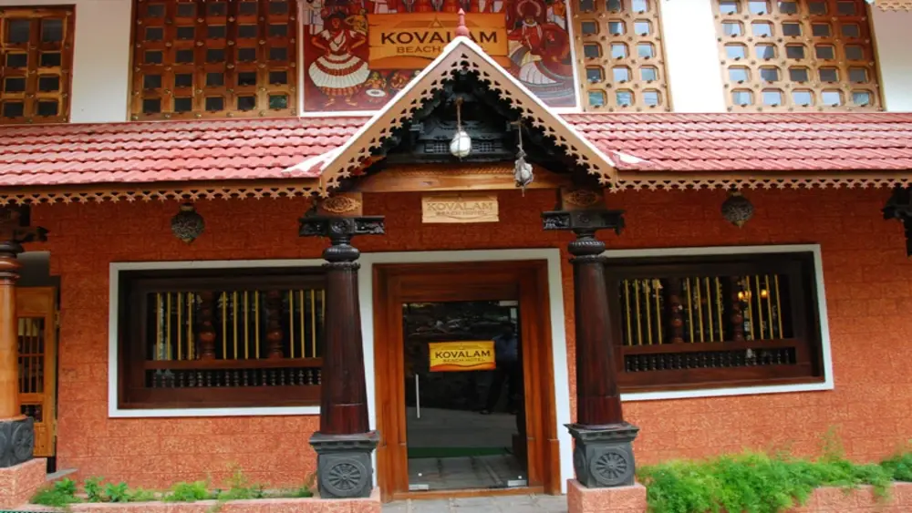 Traditional Kerala style building of Kovalam Beach Hotel featuring an ornate wooden gabled entrance and brick-red walls.