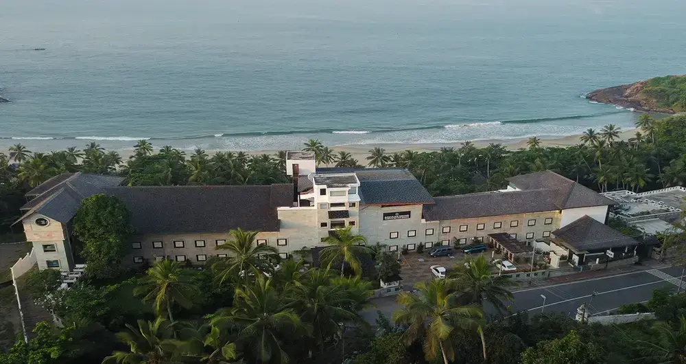 Wide angle drone view of Gokulam Grand Turtle on the Beach resort building overlooking the Kovalam coastline