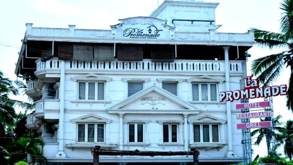Multi-story white building facade of La Promenade Hotel Kovalam with private guest balconies and palm trees.