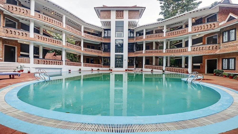 Large outdoor swimming pool in front of the multi-story guest room wings at Gods Own Country Ayurveda Resort Kovalam