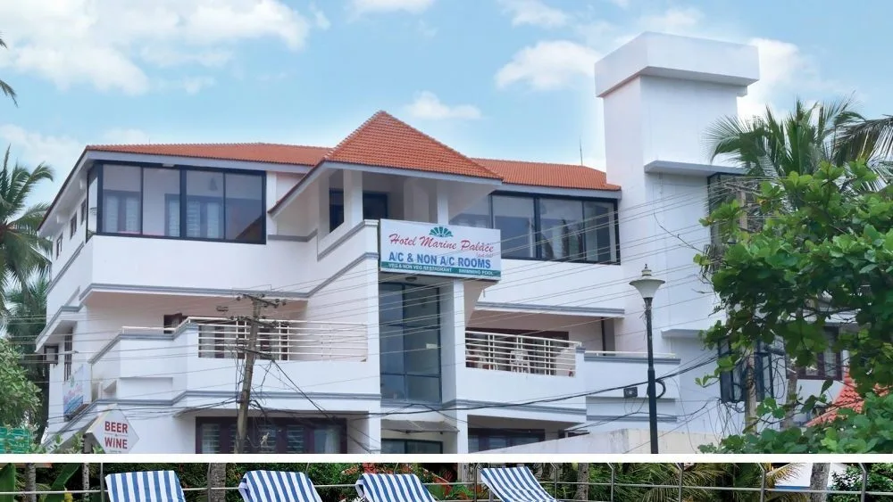Multi-story white building of Hotel Marine Palace Kovalam featuring red tiled roofs and private guest balconies.