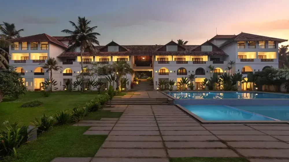 Wide angle twilight view of the illuminated luxury guest room blocks and swimming pool at Estuary Island Resort Kovalam