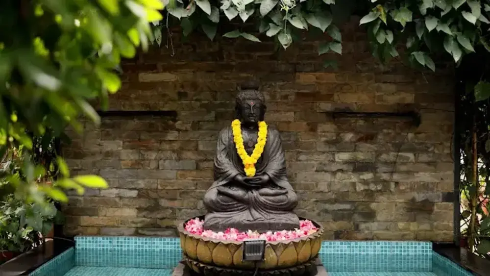 Outdoor stone courtyard at Ideal Ayurvedic Resort Kovalam featuring a Buddha statue surrounded by green tropical plants.