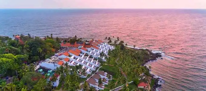 A distant view of The Leela Kovalam, A Raviz Hotel, perched on a rocky headland near Lighthouse Beach