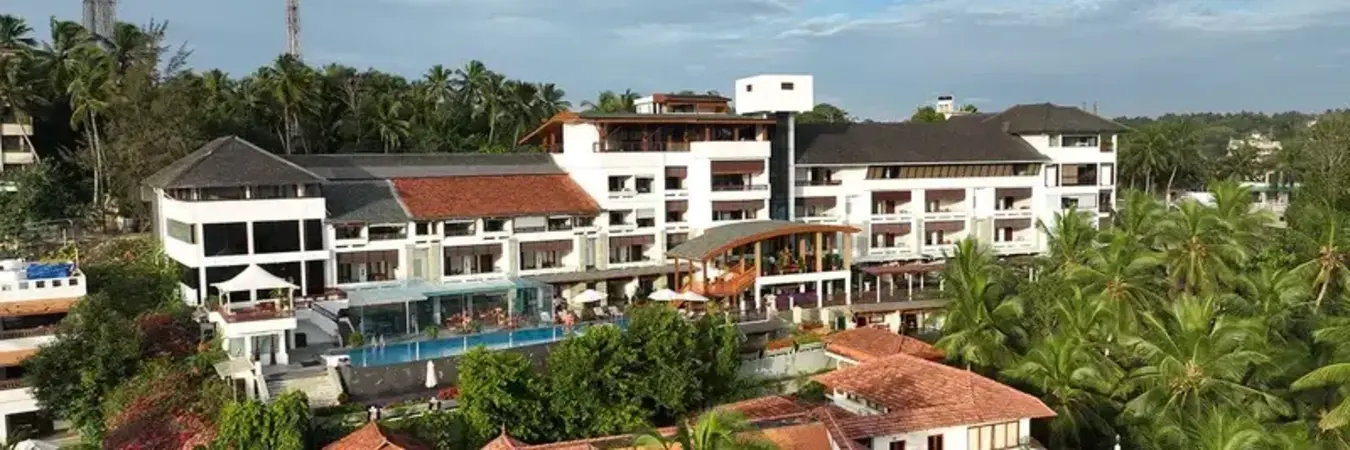 Daytime exterior view of the white resort building wings and tropical courtyard at Gokulam Grand Turtle on the Beach Kovalam