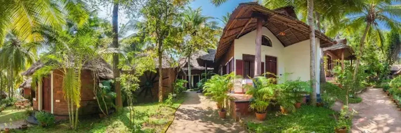 Traditional wooden and brick Kerala house style accommodation surrounded by palm trees at Soma Manaltheeram resort