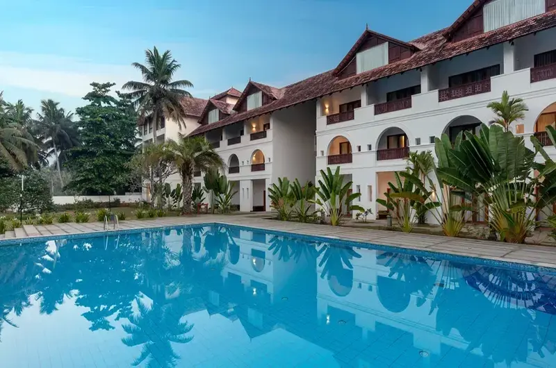 Daytime perspective of the outdoor swimming pool alongside the multi-story white building facade at Estuary Island Resort Poovar