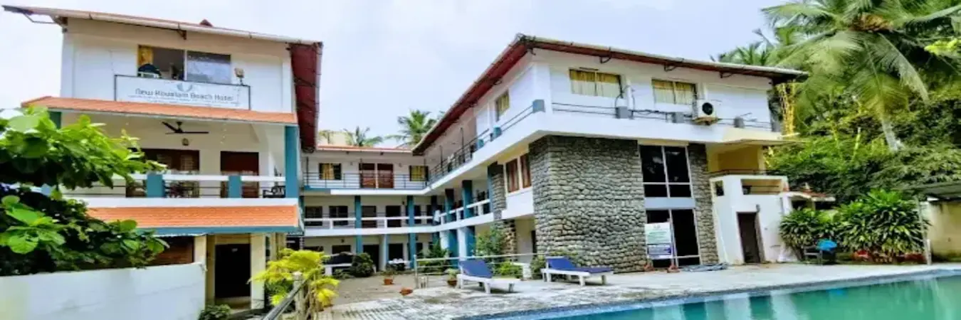 New Kovalam Beach Hotel building facade with outdoor swimming pool and guest balconies.