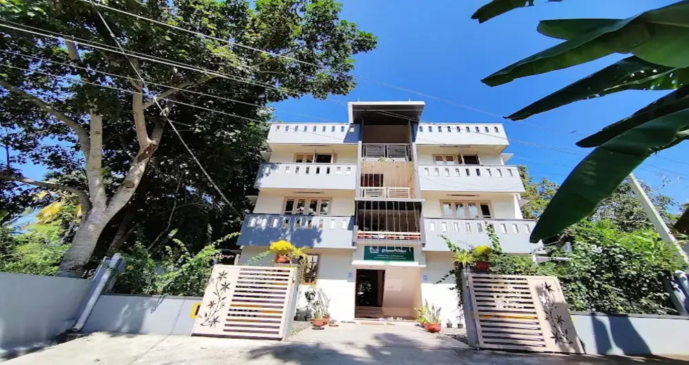 Wide angle exterior view of the multi-story Greenview Homestay Kovalam building surrounded by green tropical trees