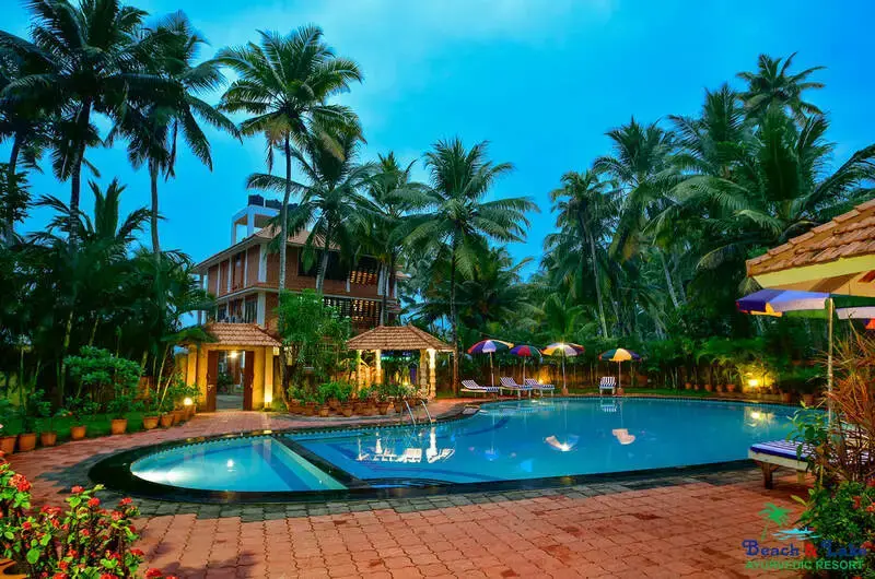 Large outdoor swimming pool at Beach and Lake Ayurvedic Resort surrounded by lush coconut trees.