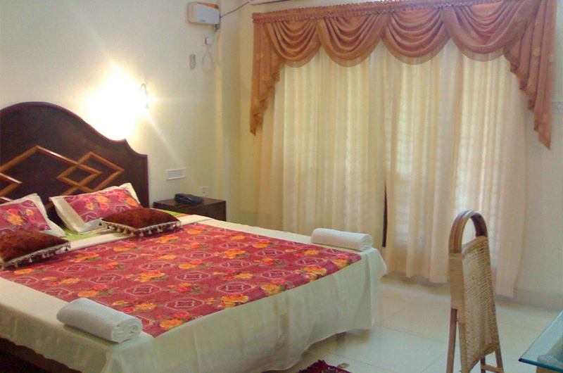 Comfortable air-conditioned guest bedroom setup with large curtains at Golden Sands Beach Resort Kovalam.