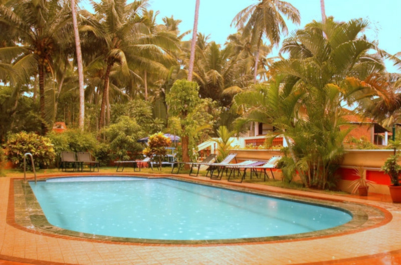 Outdoor swimming pool area at Golden Sands Beach Resort Kovalam surrounded by tropical palm trees.