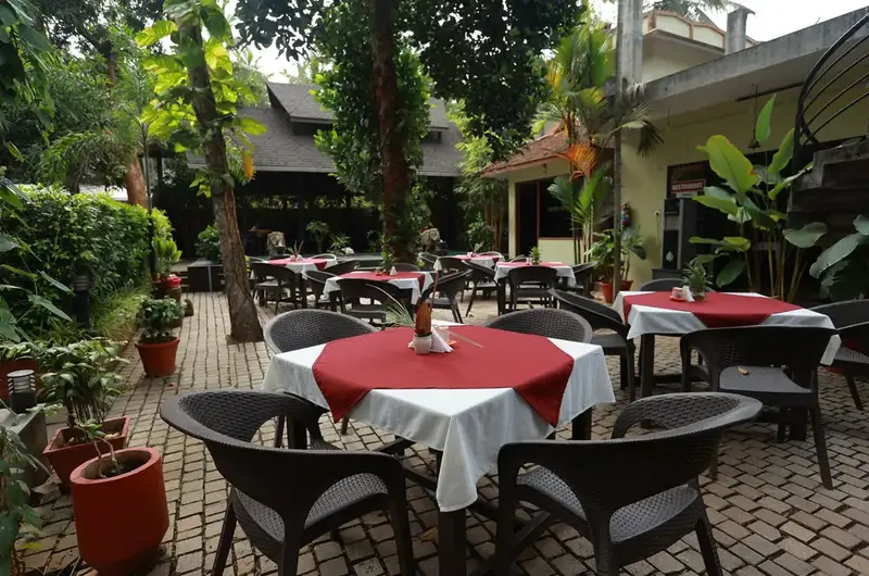 Outdoor garden restaurant and dining tables under the trees at Ideal Ayurvedic Resort Kovalam.
