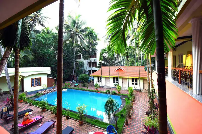 Outdoor swimming pool area at Ideal Ayurvedic Resort Kovalam surrounded by lush tropical trees.