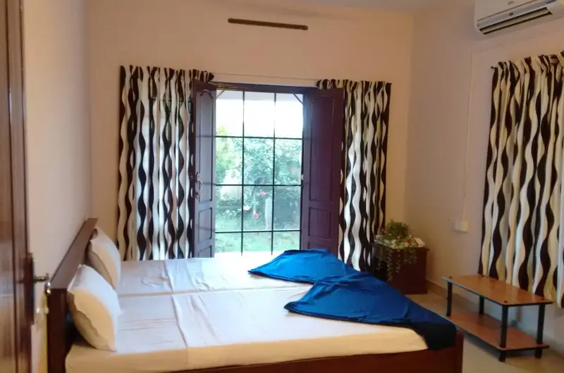 Well-appointed guest bedroom featuring comfortable bedding and wide windows at Indeevaram Apartments Kovalam.