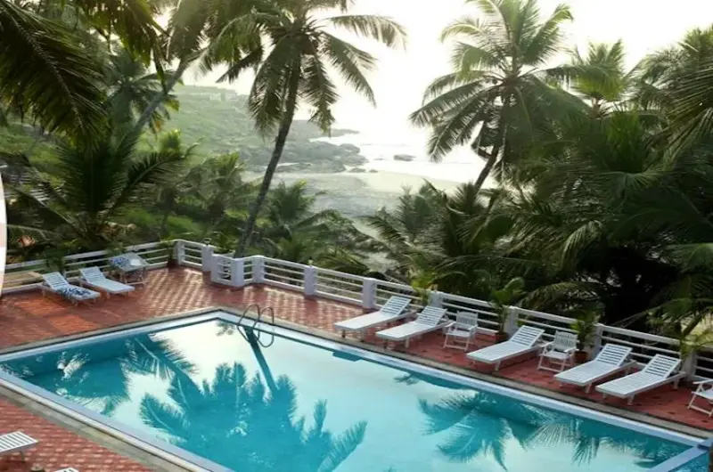 Outdoor swimming pool lined with sun loungers and tropical palm trees at Soma Palmshore Beach Resort