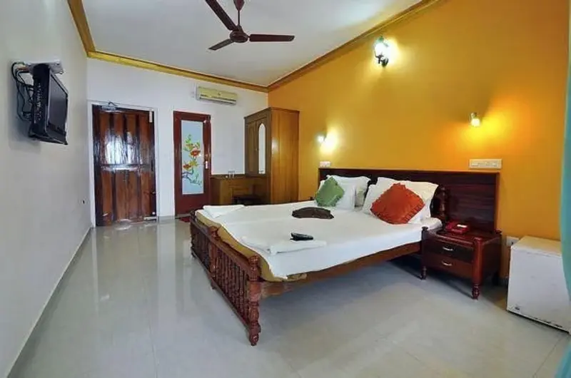 Spacious guest room with warm yellow interiors and comfortable bedding at Pappukutty Beach Resort Kovalam