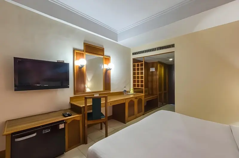 Comfortable AC guest room featuring classic wood furnishings and vanity mirror at Swagath Holiday Resort