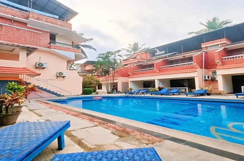 Relaxing outdoor swimming pool area at Hotel Thushara Kovalam surrounded by tropical palm trees.