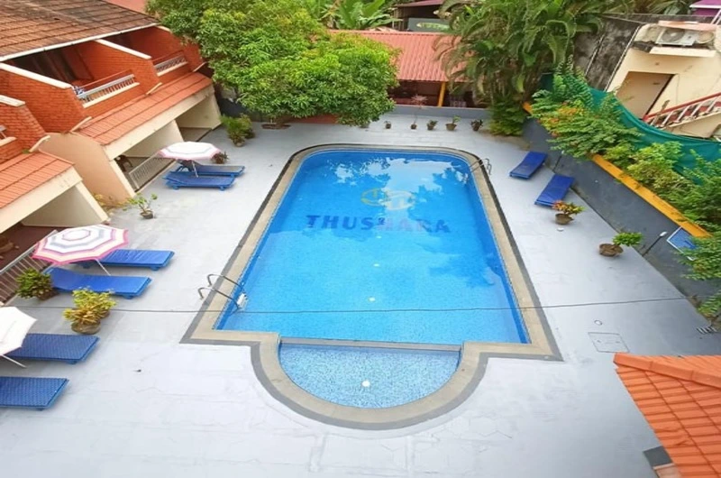 Clear outdoor swimming pool courtyard with sunbeds and loungers at Hotel Thushara Kovalam.