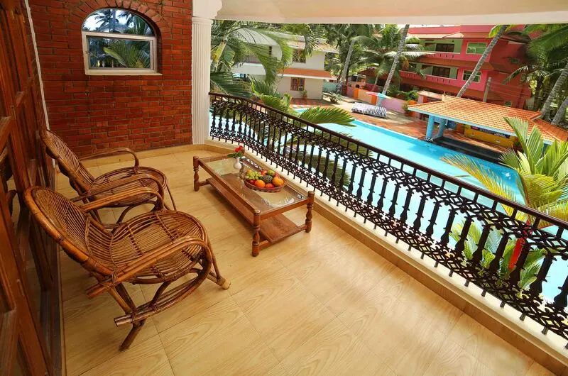 Relaxing wooden chairs on a private balcony overlooking the pool at Jasmine Palace Kovalam.