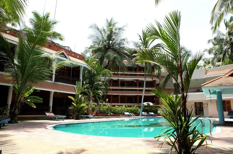 Clear blue outdoor swimming pool surrounded by tropical palm trees at Jasmine Palace Kovalam.