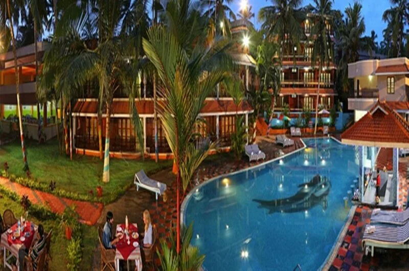 Outdoor swimming pool and illuminated multi-story resort building at Jasmine Palace Kovalam.