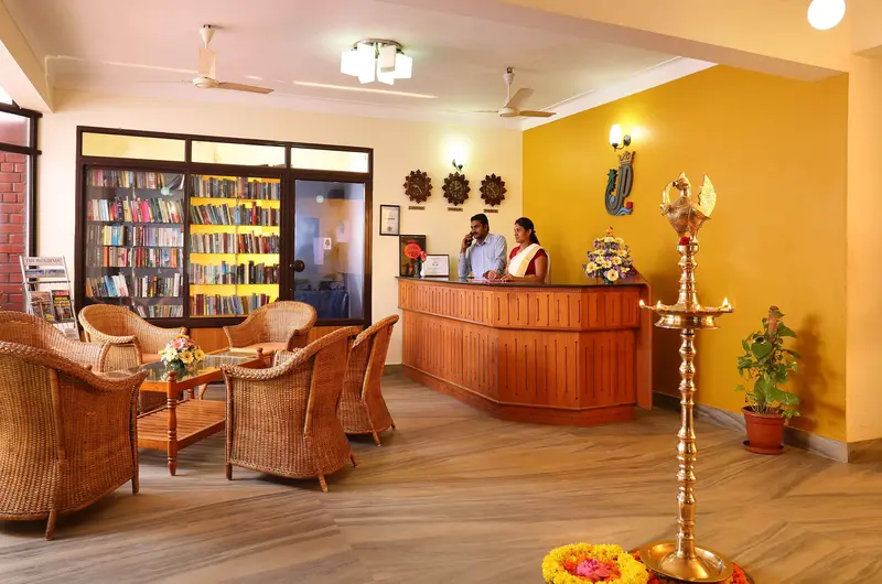 Traditional wooden reception desk and cozy indoor lobby lounge area at Jasmine Palace Kovalam.