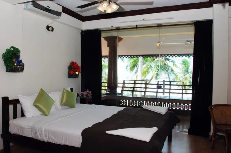 Premium double bedroom interior leading to an outdoor balcony at Kovalam Beach Hotel.