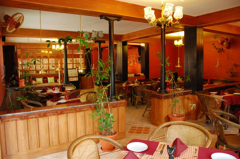 Indoor multi-cuisine restaurant and guest dining hall with warm lighting at Kovalam Beach Hotel.