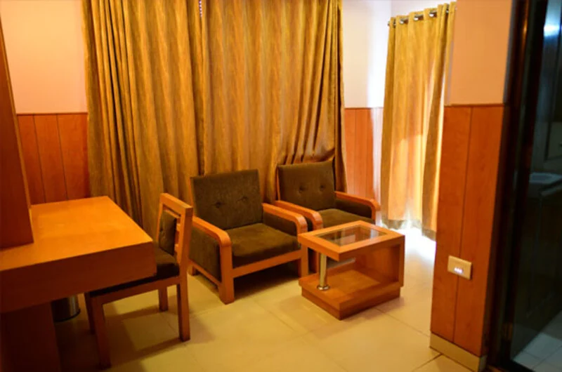 Comfortable guest living room lounge with wooden chairs and warm lighting at La Promenade Hotel Kovalam.