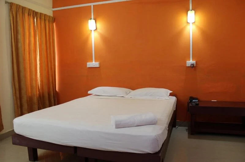Elegant deluxe double bedroom interior featuring clean linens and a window view at New Kovalam Beach Hotel.