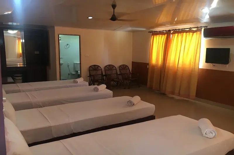 Spacious premium triple bedroom accommodation with warm wooden wall paneling at New Kovalam Beach Hotel.