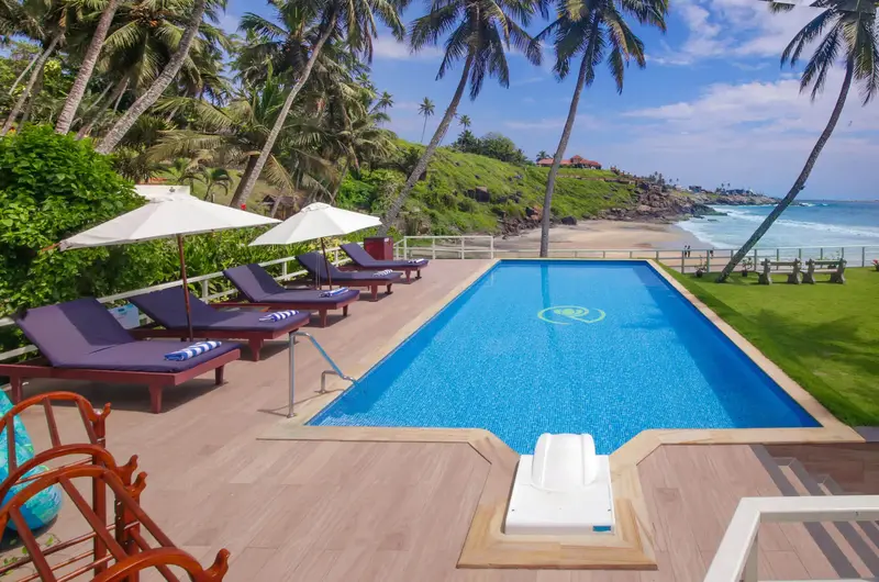 Premium poolside relaxation deck with lounge chairs and umbrellas at Rockholm Ayurveda hospital.