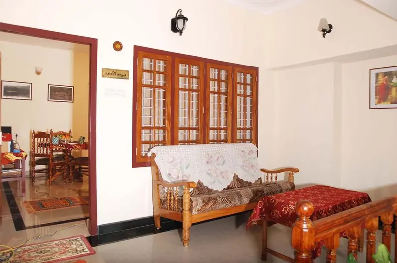 Cozy common sitting lounge featuring traditional wooden sofas and glass windows at Devikripa Homestay Kovalam.