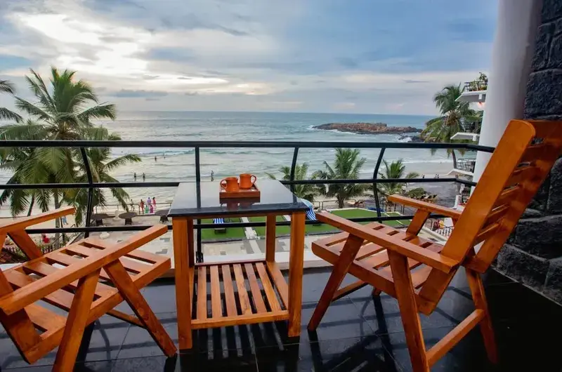 Private balcony seating area with wooden chairs overlooking the ocean at The Neelakanta Beach Resort Kovalam.