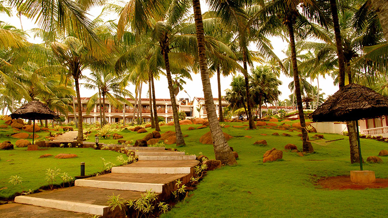Lush green garden pathway lined with coconut trees at Samudra KTDC Kovalam