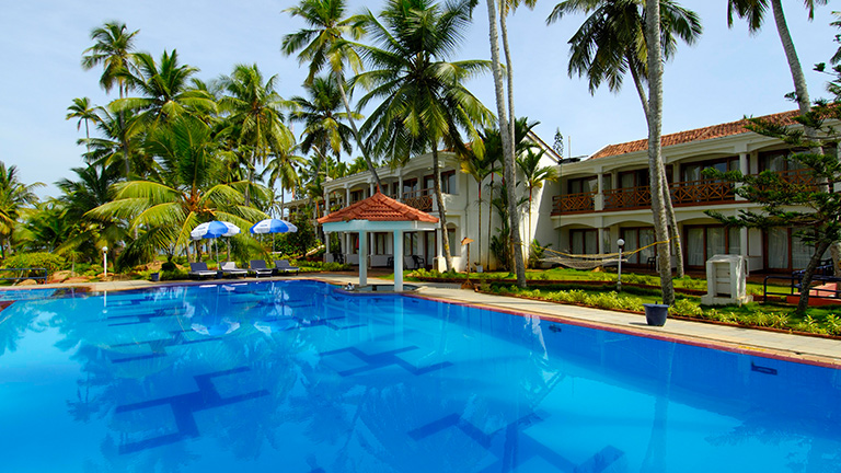 Large outdoor swimming pool surrounded by palm trees at Samudra KTDC Kovalam