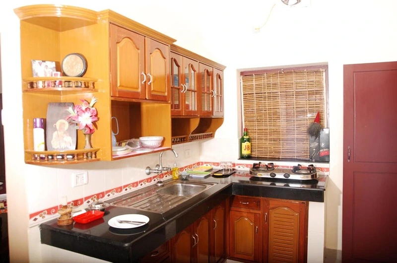 Clean shared kitchen space with wooden cabinets and polished granite counter at Devikripa Homestay Kovalam.