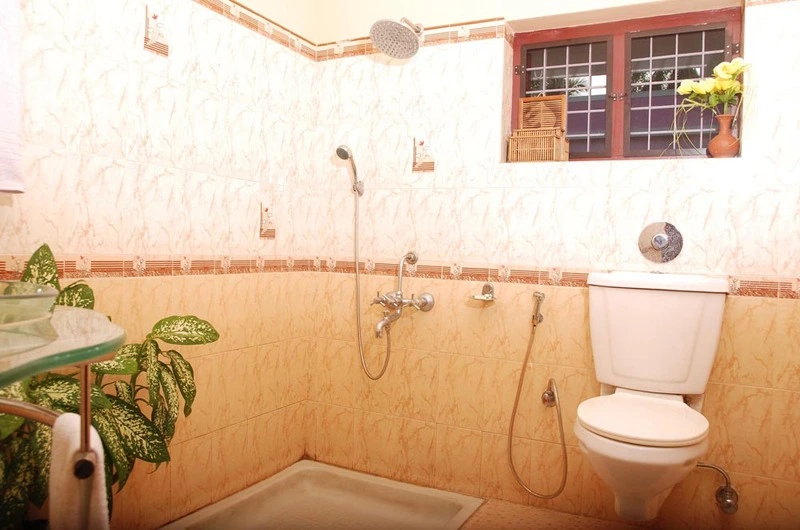 Clean attached guest bathroom interior featuring modern beige wall tiles and a western toilet at Devikripa Homestay Kovalam.
