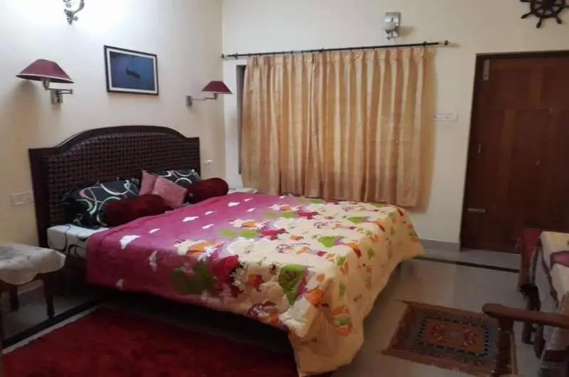 Deluxe guest room layout featuring a clean double bed and traditional dark wood furnishings at Devikripa Homestay Kovalam.